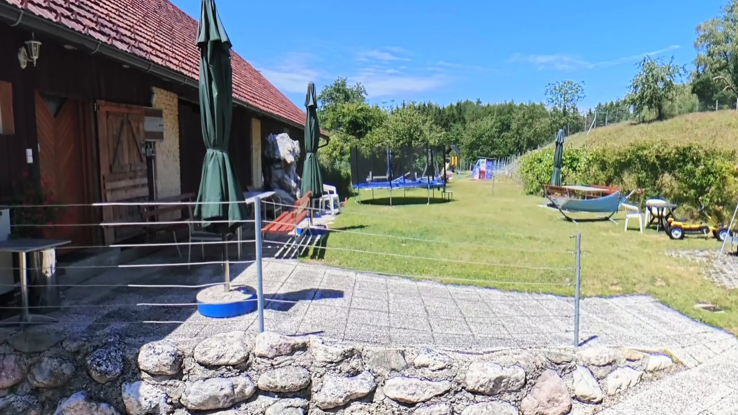 Terrasse und Innenhof mit Sonnenschirmen, dahinter die Spielwiese