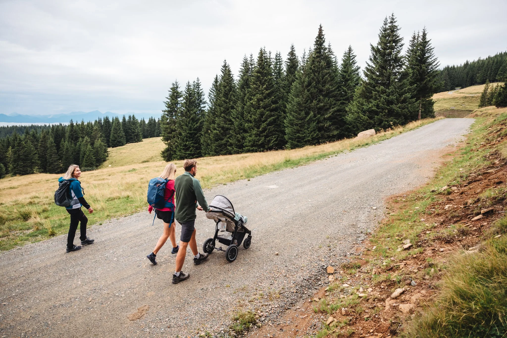 Familie schiebt einen Kinderwagen über einen breiten Schotterweg auf der Brandlalm