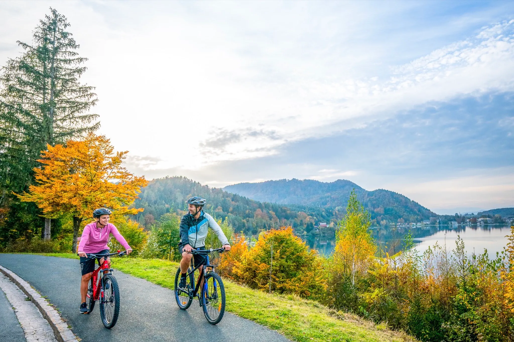 Radfahrer auf dem Uferweg im Herbstlicht, dahinter der See