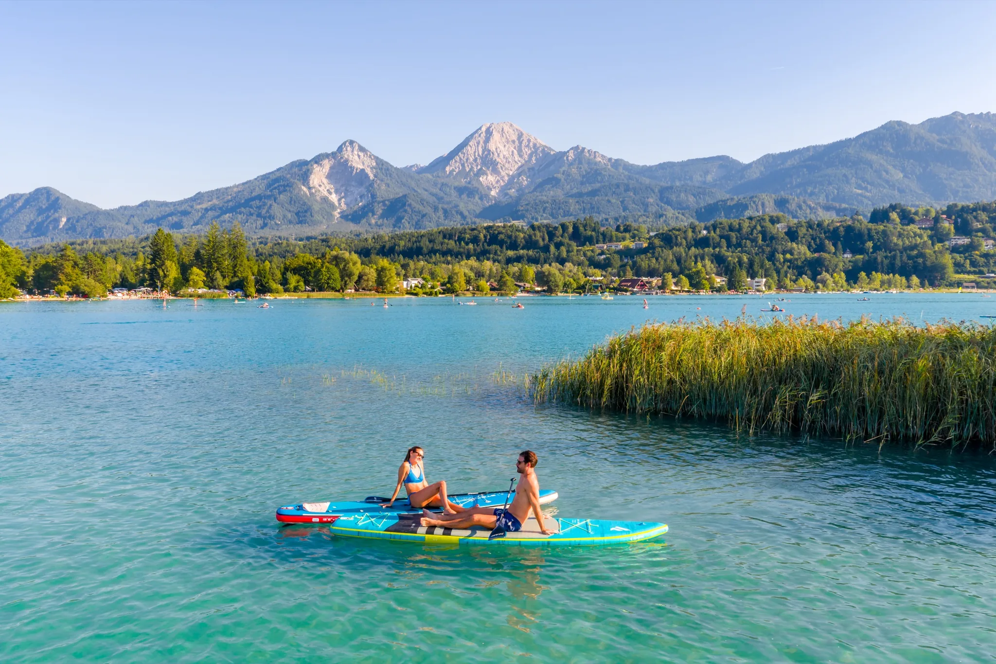 Stand-up-Paddler auf dem türkisen Faaker See, dahinter der Mittagskogel