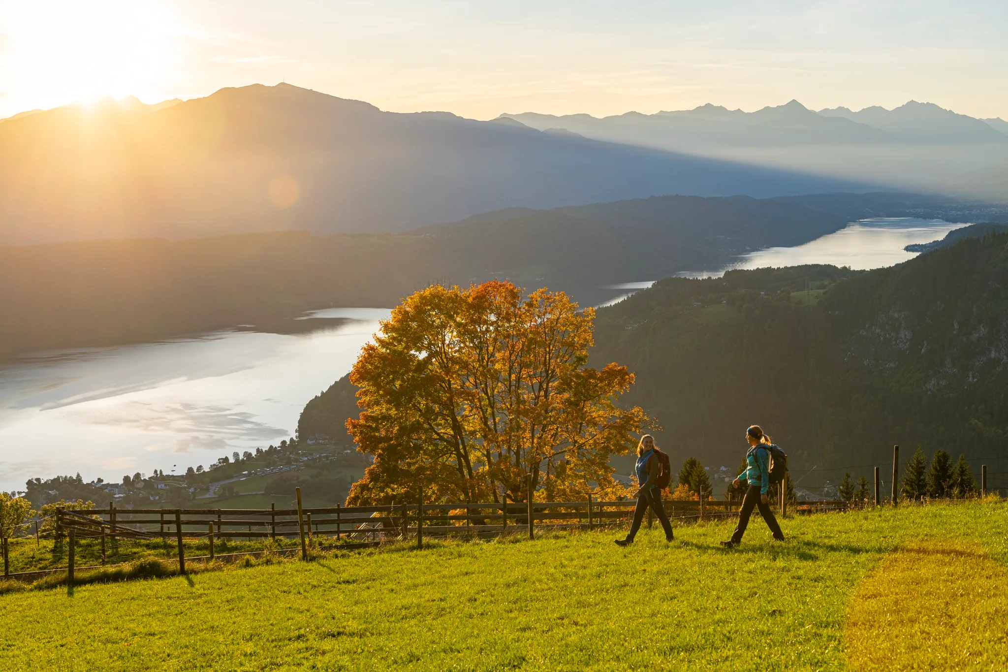 Zwei Wanderer auf einer Wiese hoch über dem Millstätter See im Herbstlicht