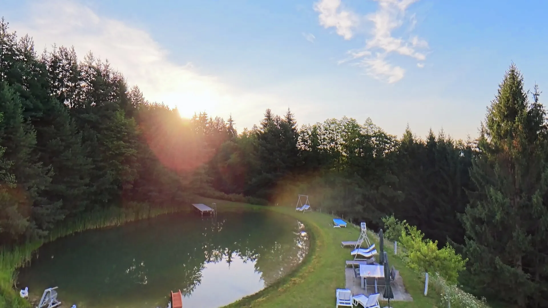 Morgensonne über dem Naturteich, mit Steg und Liegestühlen am Ufer