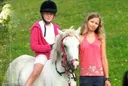 Zwei Mädchen mit dem weißen Hofpony auf der Blumenwiese